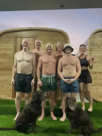A group standing in front of the cedar sauna with two dogs on the grass